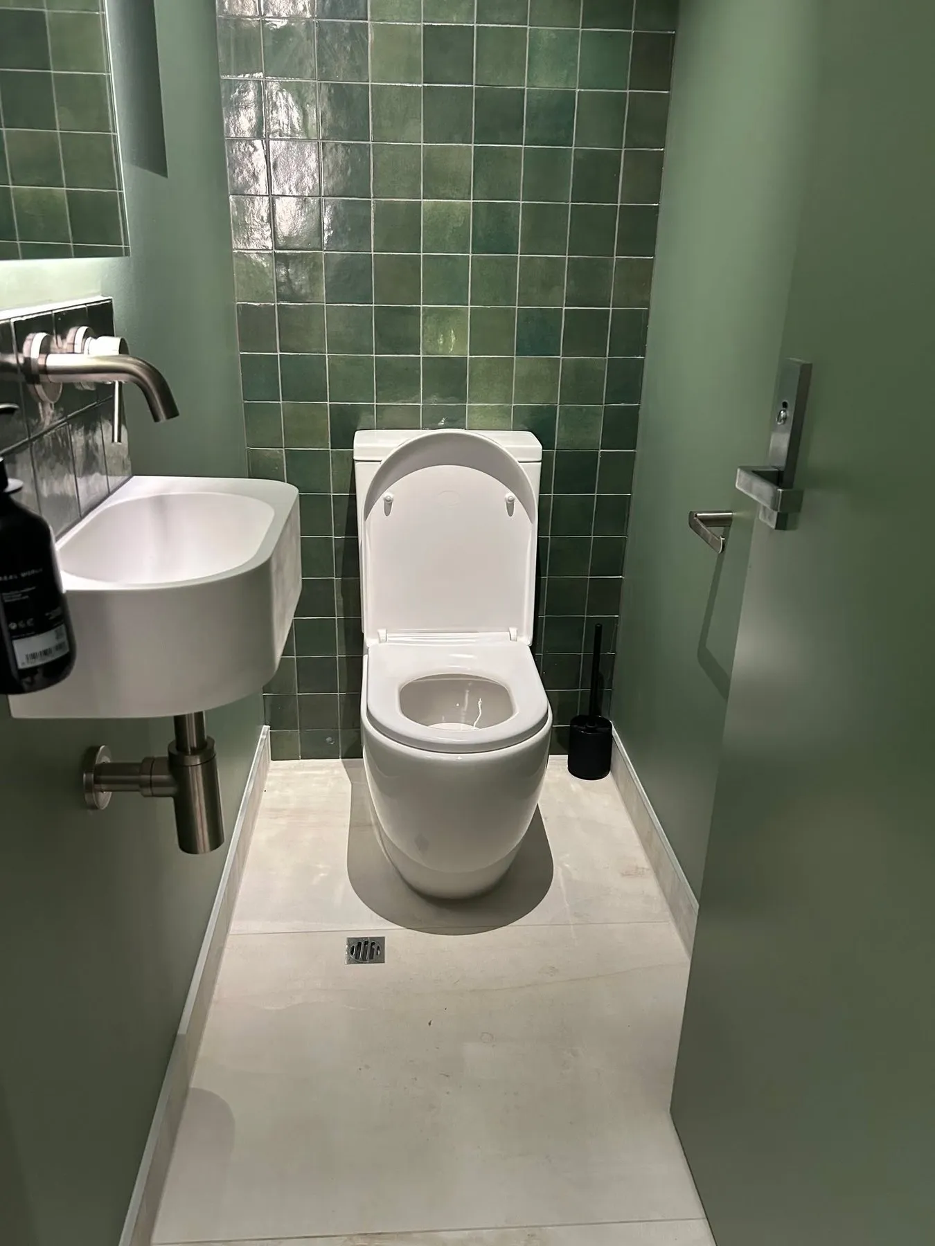 A finished Napier bathroom with a new toilet installed against green tiles and a wall hung basin