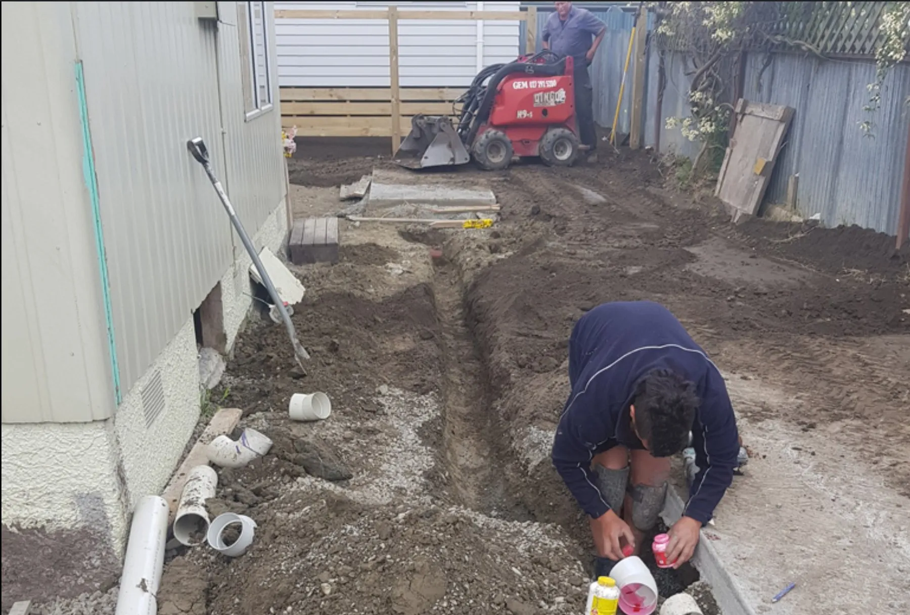 New drainage being laid in an open trench beside a Napier house, with a mini loader and PVC pipe on site