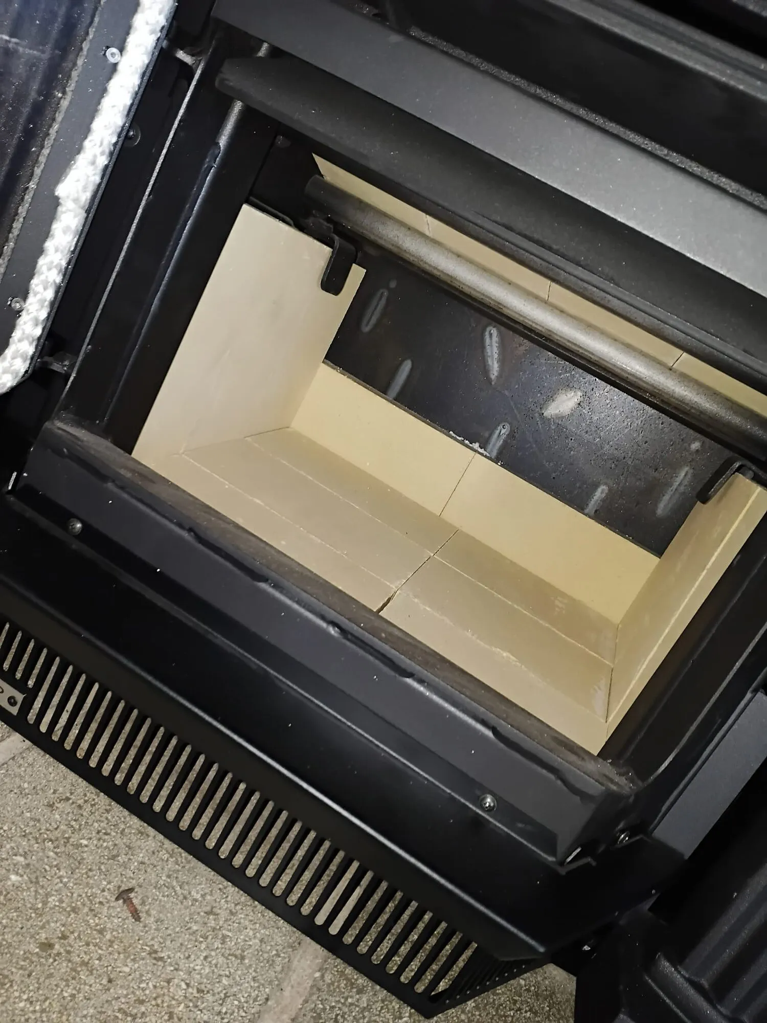 Close up inside an inbuilt wood fire, showing clean cream firebox lining panels and the baffle above