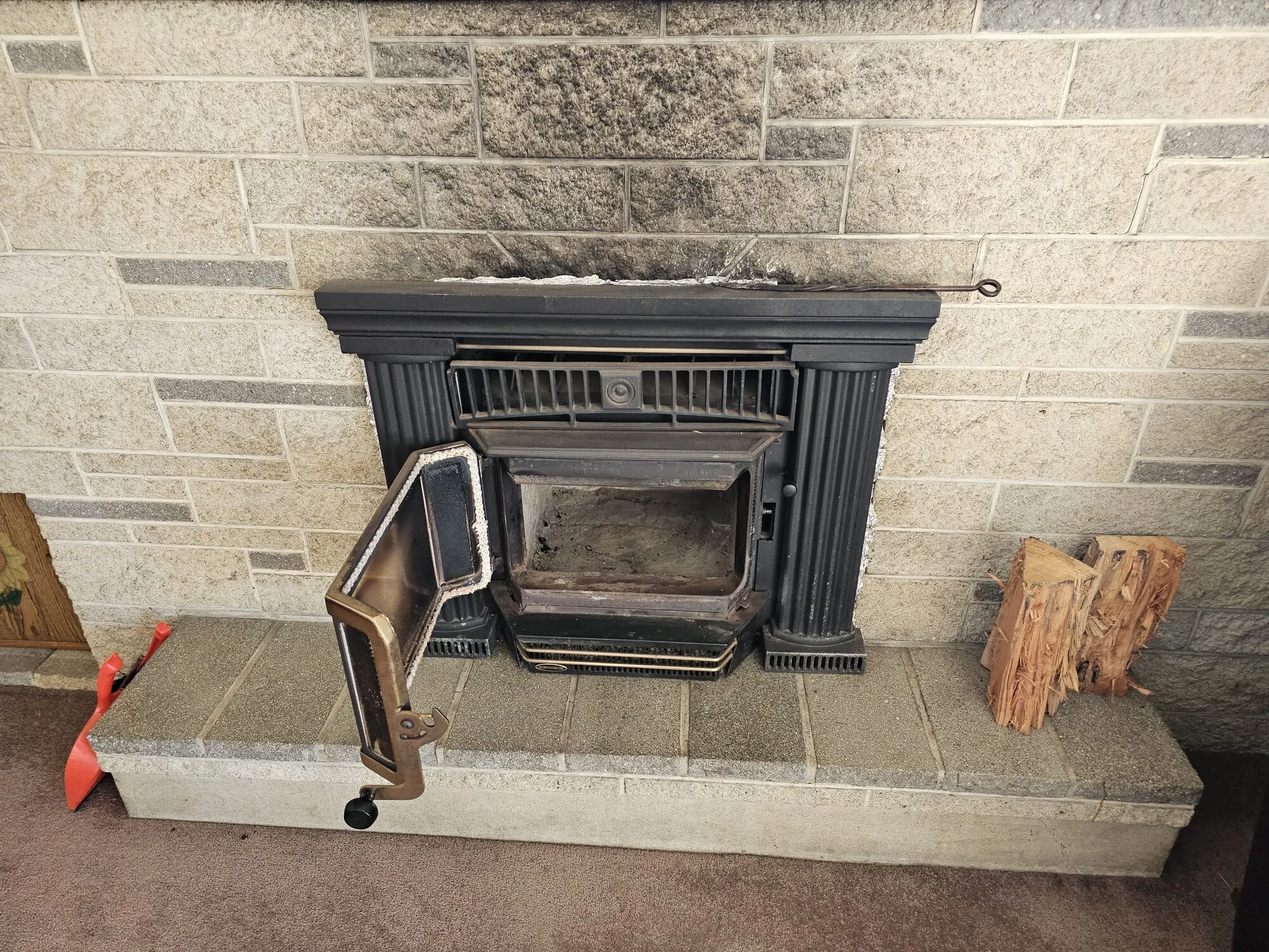 An old inbuilt wood fire in a stone fireplace with its door hanging open, soot stained stonework above it and split kindling on the hearth