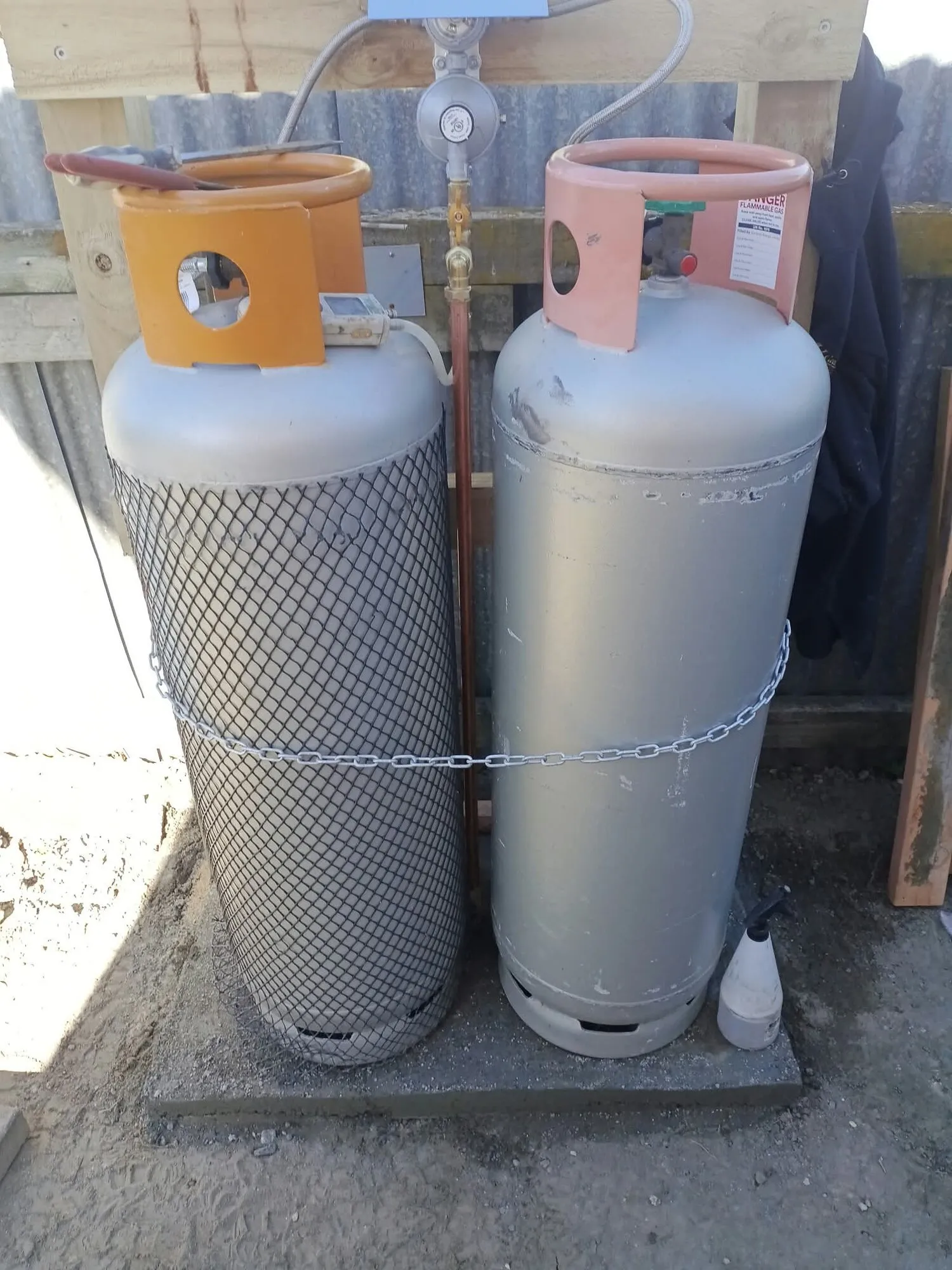 Two 45kg LPG bottles installed on a concrete pad beside a house, chained in place and connected through a changeover regulator