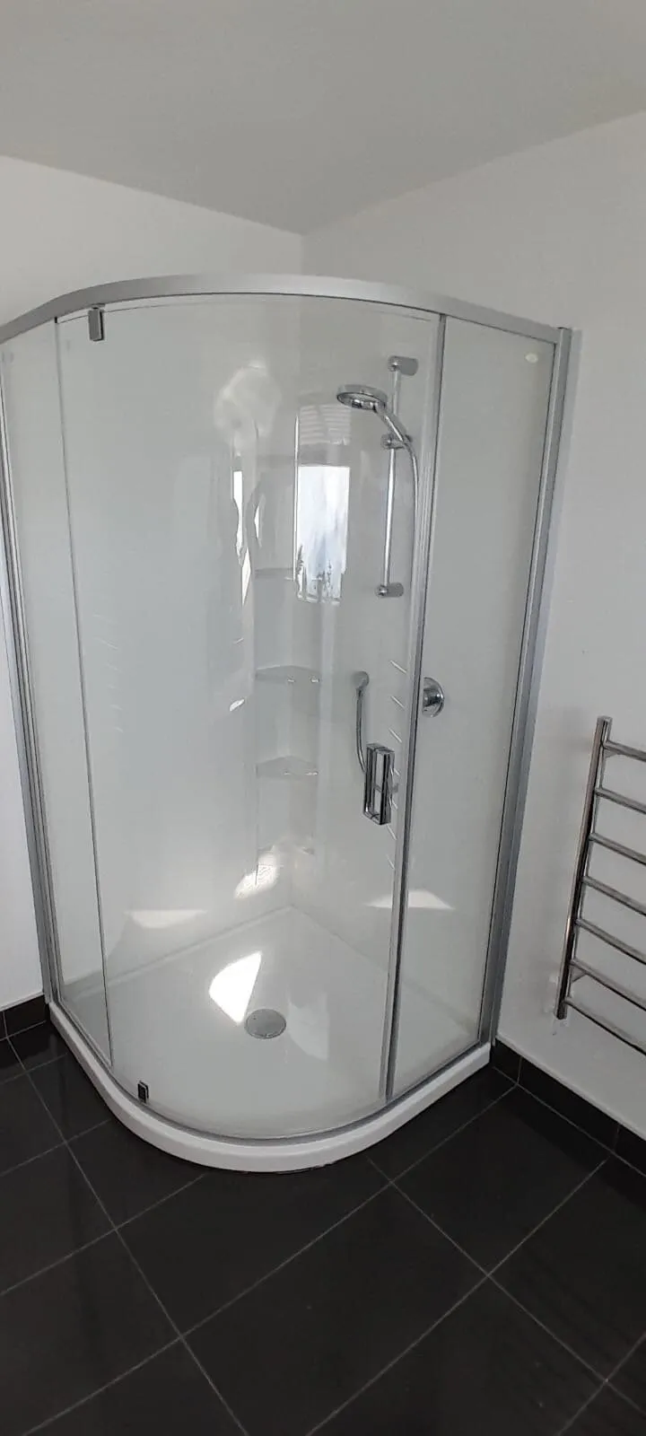 A newly installed corner shower with curved glass doors and a heated towel rail alongside, in a Hawke's Bay home
