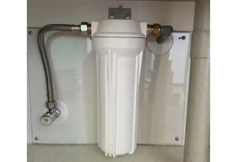 A water filter housing mounted under a kitchen sink, plumbed in with a braided supply line and isolating valve